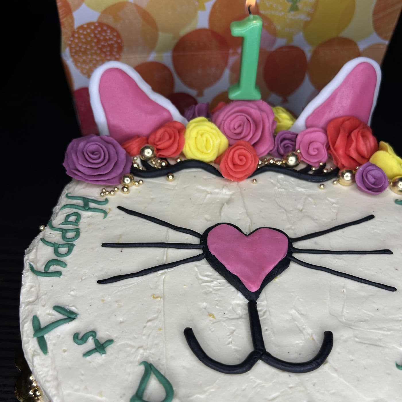 First birthday cake decorated as a cat's face, with pink fondant ears, a crown of sugar roses and a number-one candle