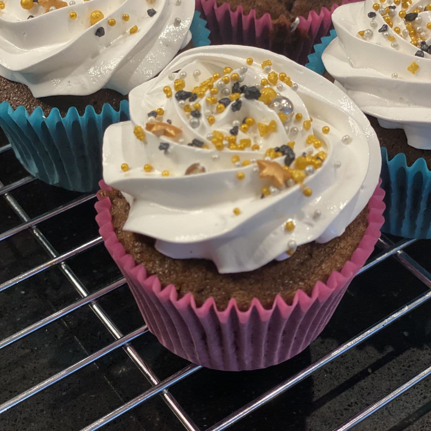 Close view of a handmade chocolate cupcake in Peterborough with a tall rose-piped buttercream swirl and gold, silver and black sprinkles