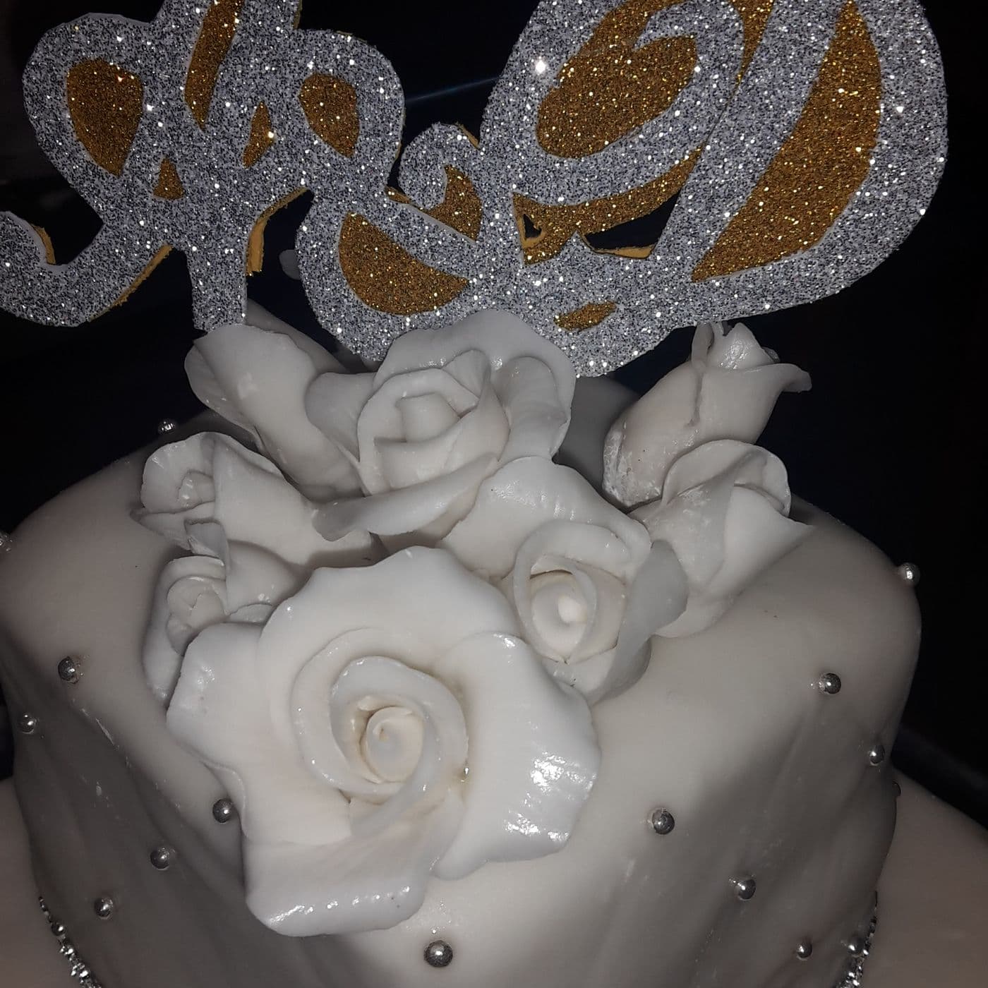 Hand-made monogram topper in silver and gold glitter above a cluster of white sugar roses on the top tier