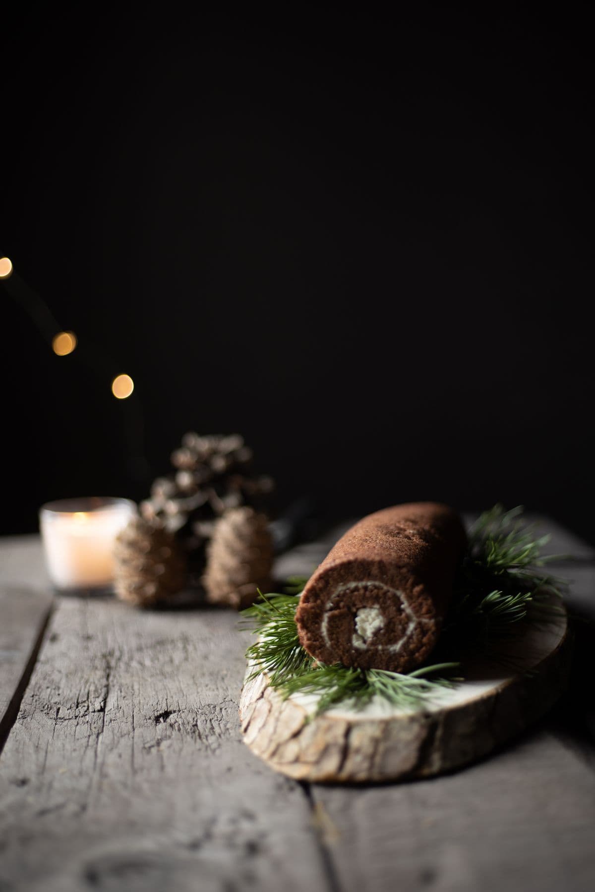 A chocolate cake roll on a rustic wooden plank with pine decorations